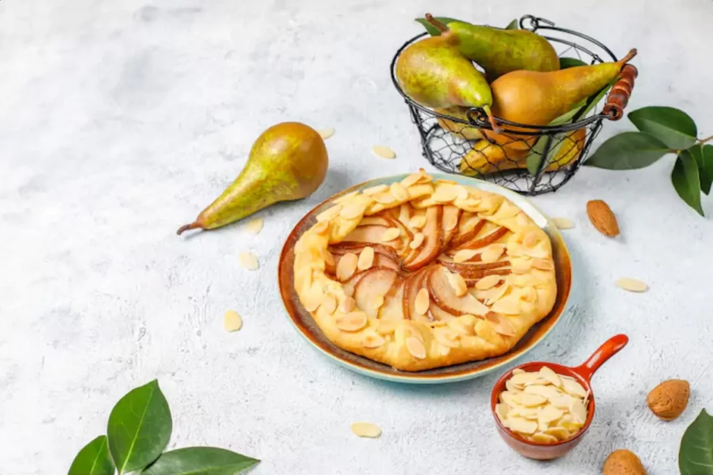 Homemade pear galette pie with almond leaves and fresh ripe green pears