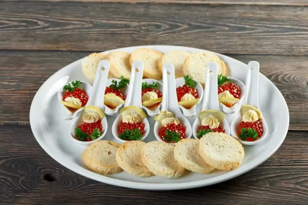 A close-up with a delicios snacks, prepeared for restaurant banquet. A big plate on the wooden table,served with a white bread, red caviar and lemons. A snack looks very tasty.