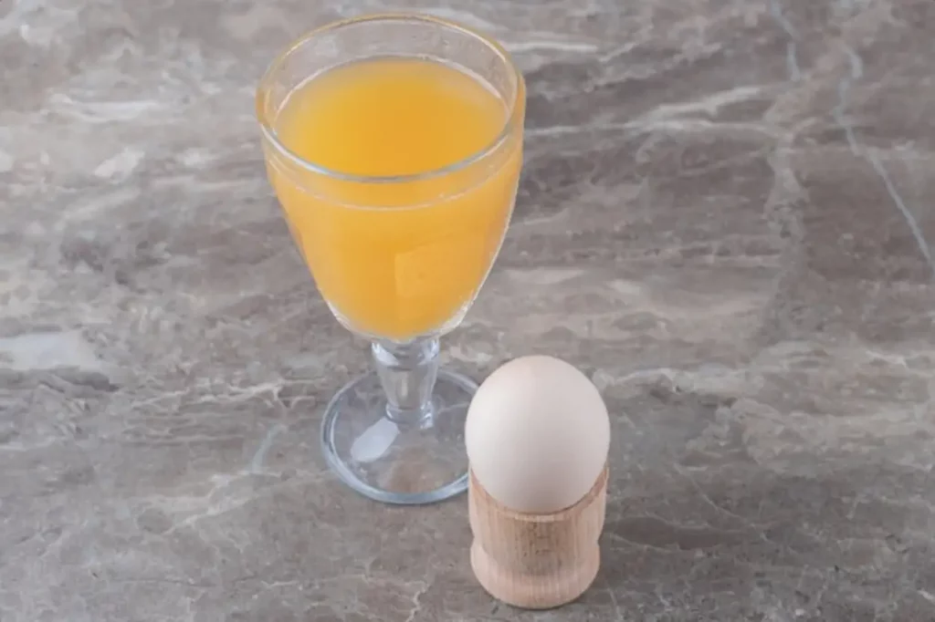 Glass of juice and boiled egg on marble table.