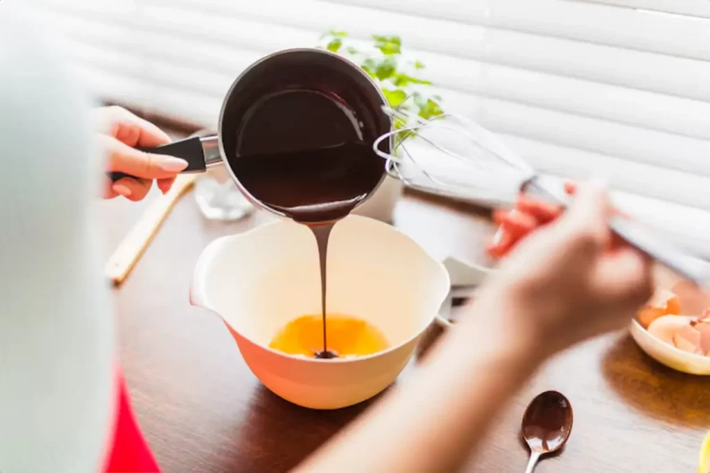 Crop woman pouring chocolate sauce into eggs