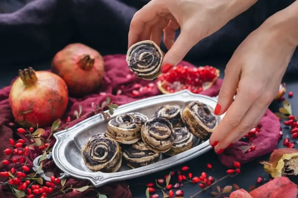 Female hands taking raw vegan puppy roll from a metal plate with rosehips and pomegranate seeds