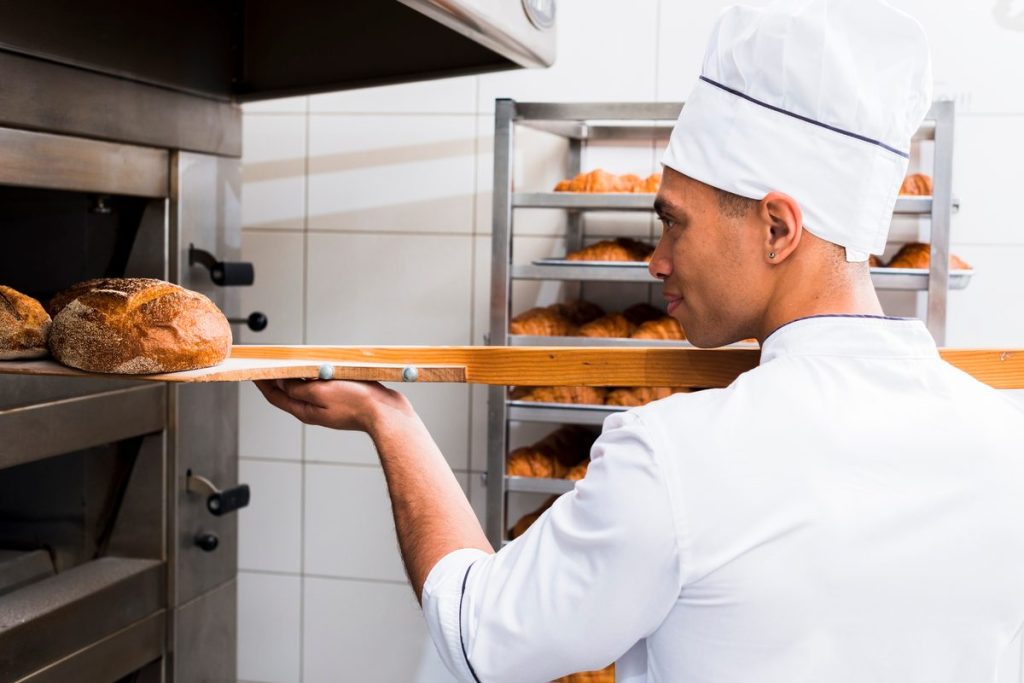 Boulanger professionnel défournant des pains de campagne à la pelle dans un fournil